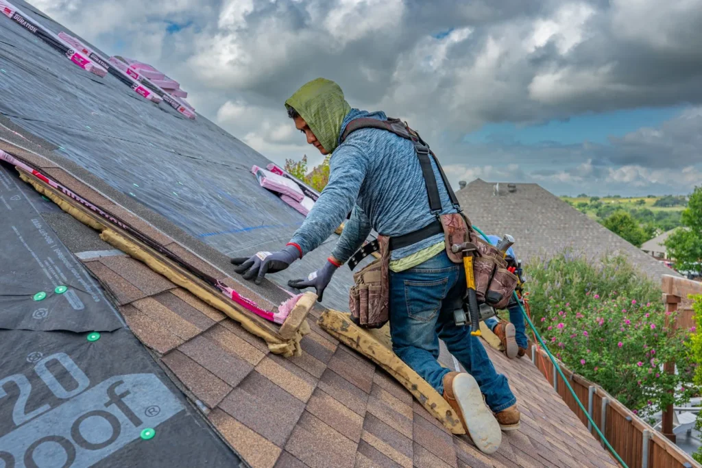 Roofer in a safety harness installing asphalt shingles along a roof slope