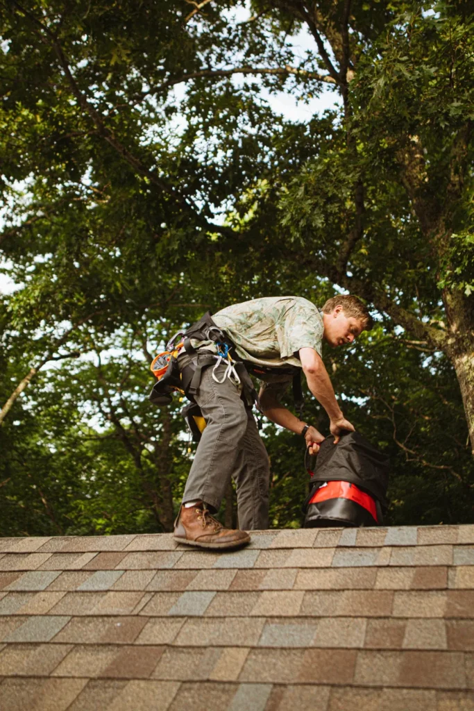 Roofer in a safety harness standing on an asphalt shingle roof