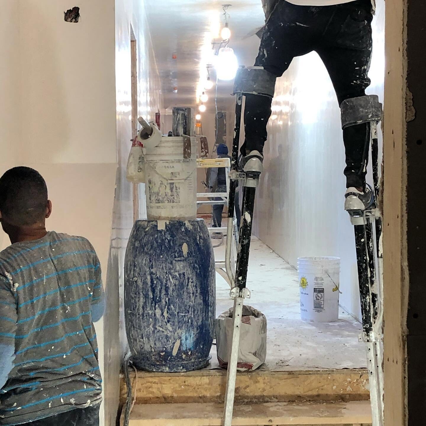 Plasterer on stilts skim-coating a ceiling and wall